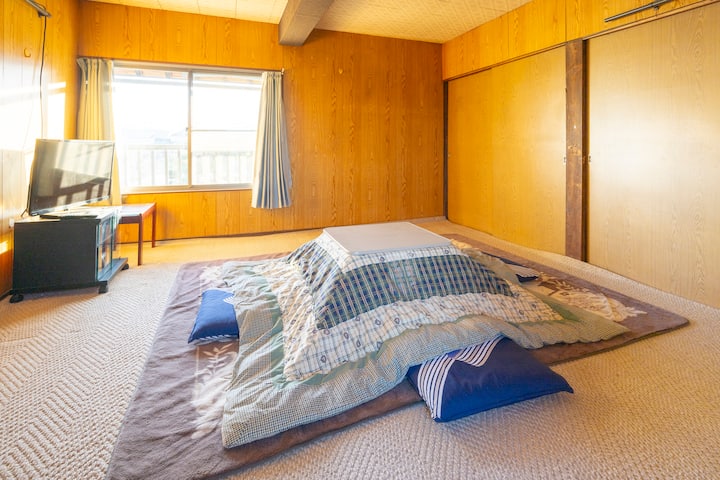 「いますわの宿」203号室
冬のコタツを設置した状態です。
TV、机、押し入れ収納、鍵付きの部屋です。お寝すみの際は、引き出しから布団を出してご利用ください。布団で最大3名様までご利用できます。

本館の階段を上がって、西側の古民家棟2Fの西側にある部屋です。本館2Fに、共用の洗面台と、トイレがあります。また西側から古民家棟1Fへ降りる階段がありますので、そこから1F古民家棟トイレもご利用できます。