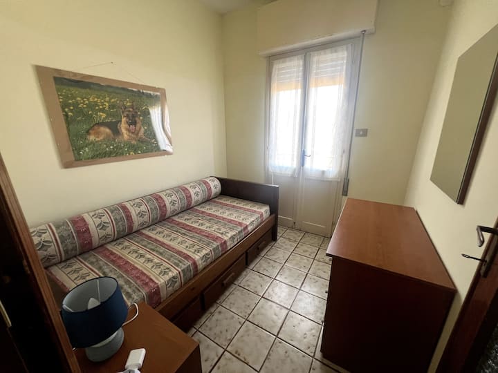 This is the smallest bedroom, upstairs. View from the door. This room has a chest of drawers and a mirror, together with a single bed and nightstand. The door opens into a small terrace.