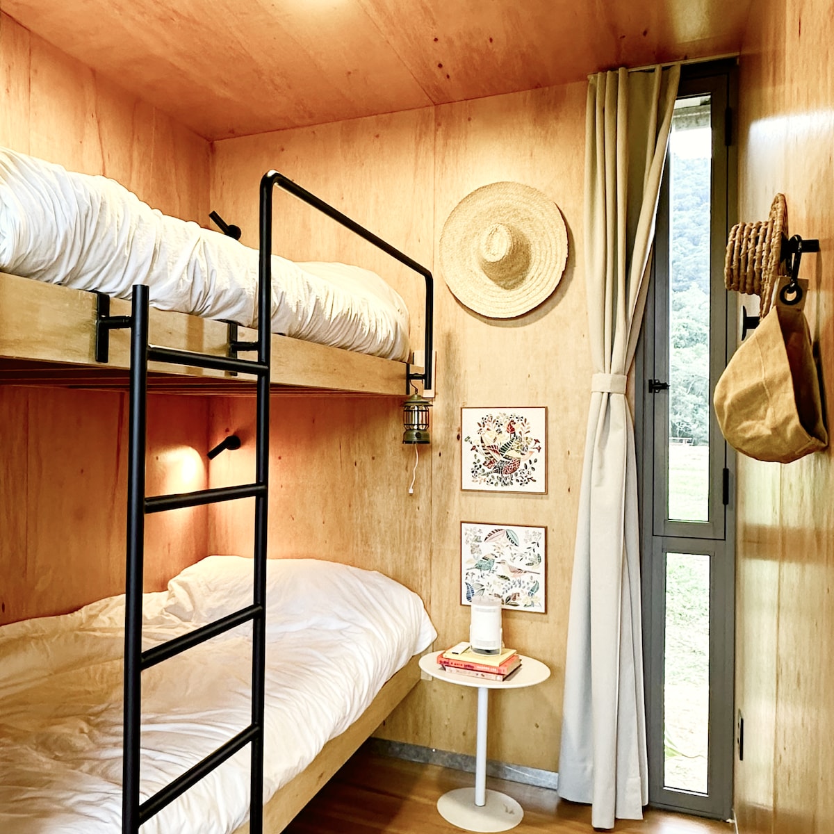 Quarto Beliche com duas camas e escada. Luminárias individuais, cortina blackout, ganchos, luminária e livros.