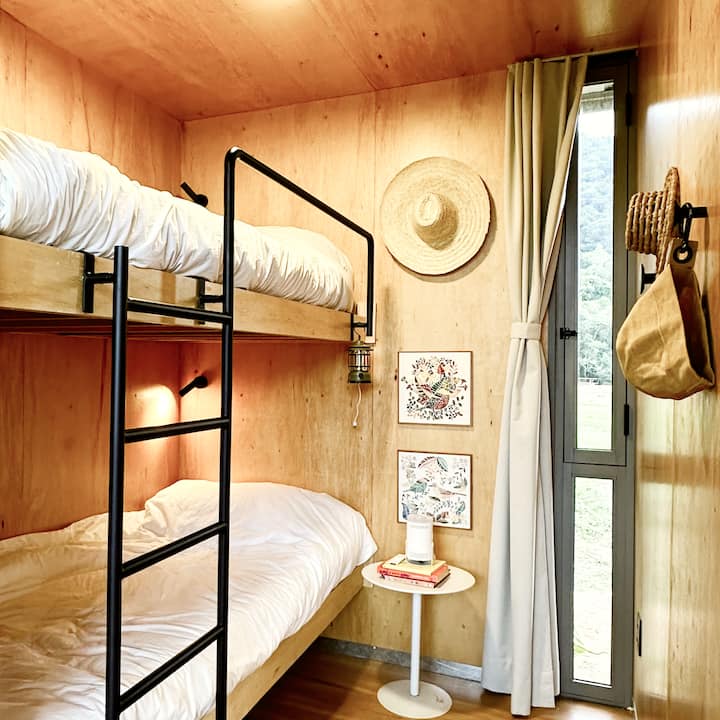 Quarto Beliche com duas camas e escada. Luminárias individuais, cortina blackout, ganchos, luminária e livros.