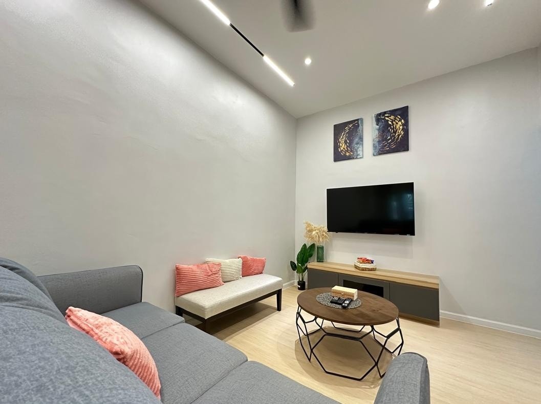 A modern living area features a comfortable sofa with accent pillows and a light-furnished coffee table. Wall-mounted artwork complements the neutral walls, while a flat-screen TV is positioned above a minimalist media console. Soft lighting enhances the spacious feel of the room.