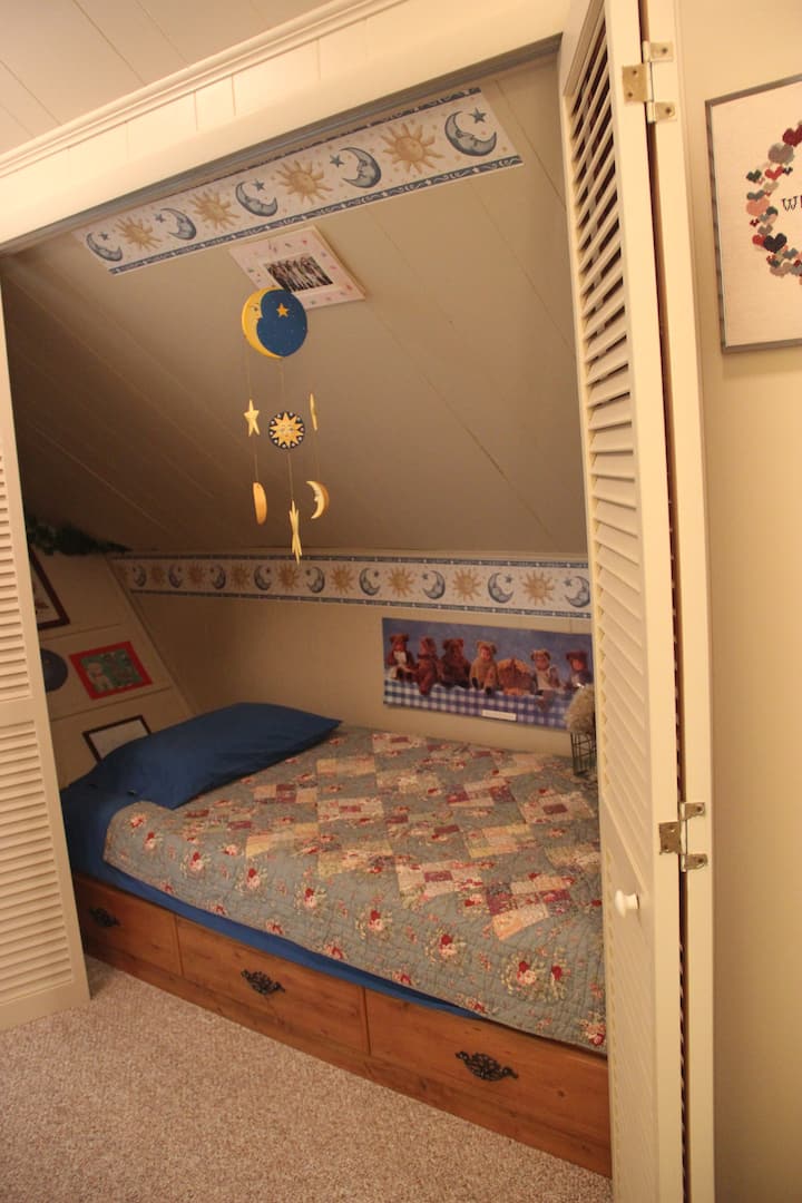 Cama de almacenamiento individual con dos cajones, ubicada en una alcoba, con puertas plegables. 
