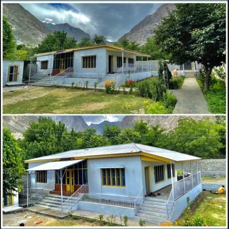 A spacious home is surrounded by lush green gardens, showcasing a sturdy railing along the porch. The architecture reflects a simple design with multiple windows allowing natural light in. Majestic mountains rise in the background, enhancing the serene setting.
