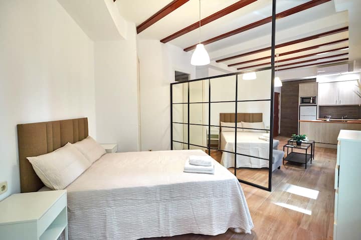 Спална соба со двоен кревет, одделена со огледало во дневната соба.