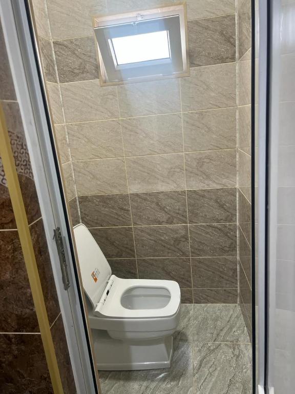 A functional bathroom space is depicted, featuring a modern toilet positioned against tiled walls in neutral tones. Natural light filters through a small window, highlighting the clean lines and simplicity of the design.