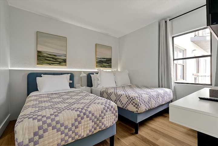 חדר שינה מואר ופונקציונלי עם מיטה זוגית ומיטת יחיד, אידיאלי למשפחות או לקבוצות קטנות. כולל טלוויזיה המורכבת על הקיר, תאורה טבעית מהחלון וריהוט מודרני בעיצוב מלוטש.