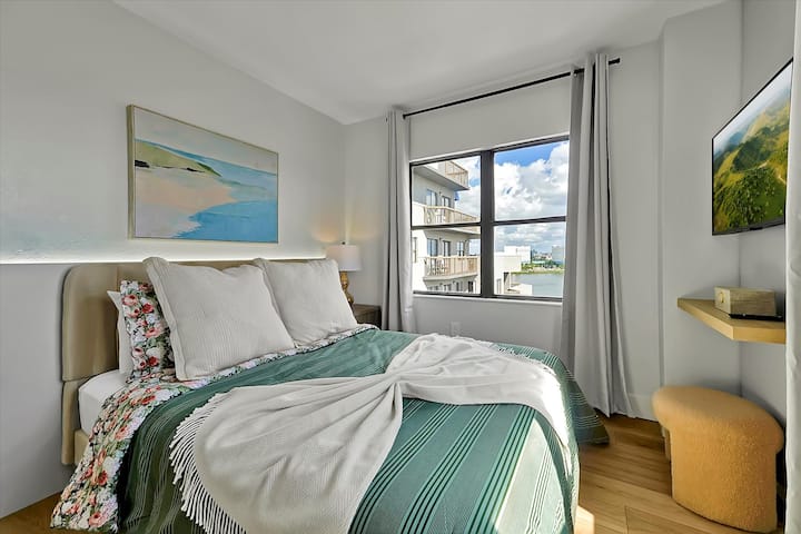 חדר שינה נעים עם מיטת קווין סייז עם מצעים רכים, שידות לילה עם מנורות וחלון גדול שממלא את החדר באור טבעי. העיצוב מינימלי ואלגנטי, ומציע אווירה שלווה ללילה רגוע.