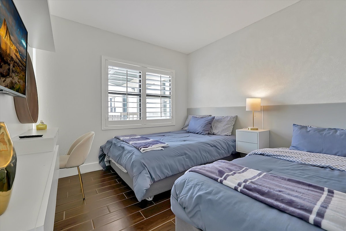 Спалня с едно двойно легло и едно единично легло, телевизор на стената, големи прозорци и меко осветление. Идеално за до 3 гости с комфорт и стил.