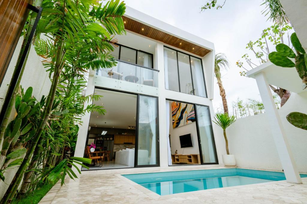 The villa's exterior showcases a modern design with large glass doors that open to the spacious living area. A private pool is visible, surrounded by lush greenery, providing a serene outdoor space. The clean lines and minimalistic architecture create a welcoming atmosphere.