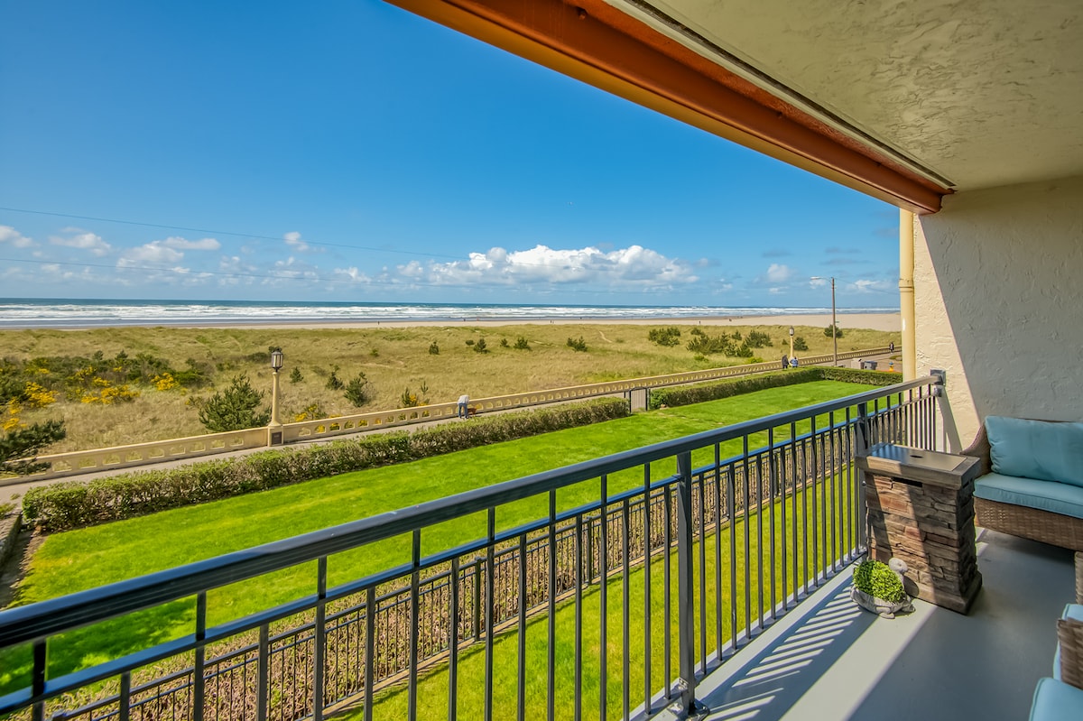 The balcony showcases unobstructed ocean views, with greenery visible along the shoreline. The space is furnished with comfortable seating and features a railing that offers a sense of safety while enjoying the fresh seaside air.