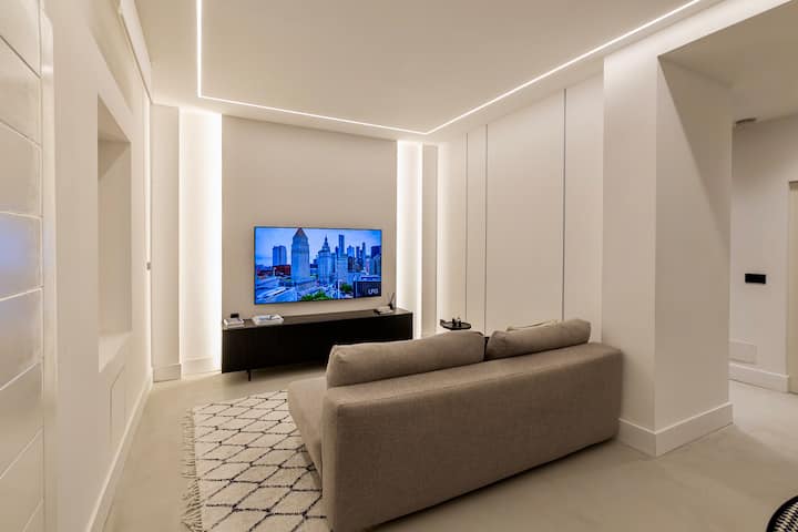 Modern living room with a comfortable sofa bed and large flat-screen TV and soft accent lighting.