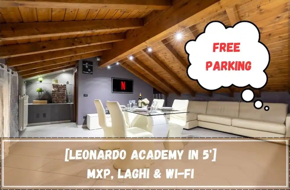 An open living area is presented with a sloped wooden ceiling, enhancing the space's warmth. A spacious white sofa is positioned near a wall-mounted flat-screen TV, which displays a red 'N' logo. Natural light fills the room, creating an inviting atmosphere.