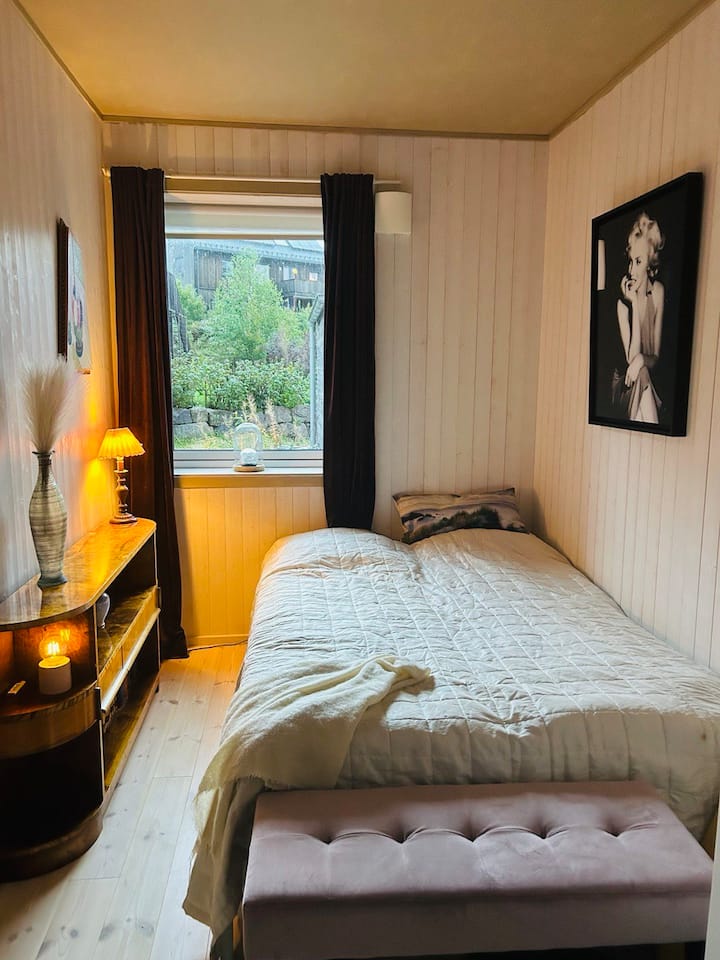 غرفة نوم بسرير مزدوج وجدران ذات ألواح مطلية بلون فاتح ونافذة.