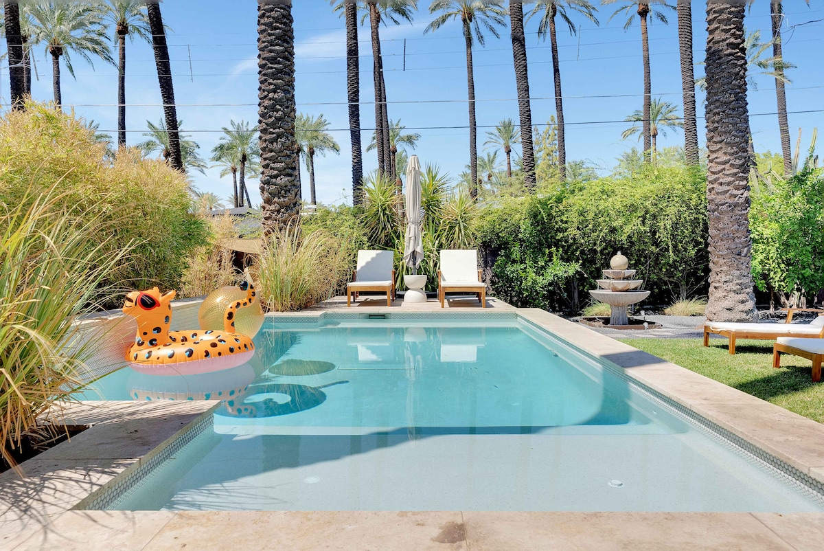 A serene outdoor space features a saltwater pool, surrounded by lush greenery and palm trees. Lounge chairs are placed beside the pool, and a playful float is positioned in the water, adding a fun element to the tranquil environment.