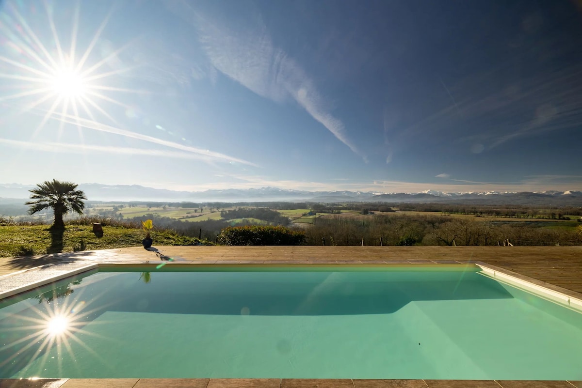A tranquil swimming pool is highlighted, reflecting sunlight and overlooking expansive rolling hills with distant mountains. The poolside is accented by a palm tree, creating a serene outdoor space ideal for relaxation. Clear skies enhance the beautiful view of the surrounding landscape.