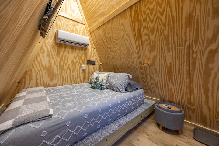 A-frame interior: comfy bed, mini-split AC/heat, and wall-mounted TV.