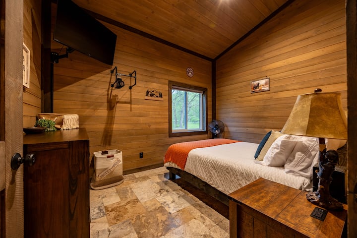 This cozy bedroom features wood-paneled walls, a plush queen bed with crisp white linens, and fun bear-themed accents.