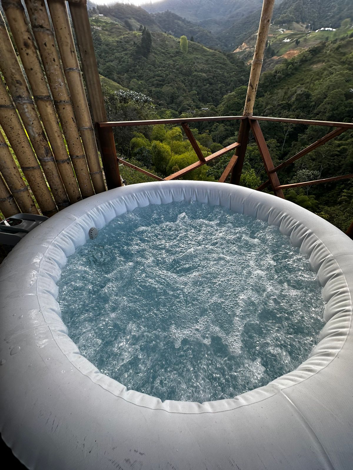 A jacuzzi filled with bubbling water is situated on a deck, offering views of surrounding greenery and mountains. The setting is designed to encourage relaxation and connection with nature, creating a tranquil atmosphere.