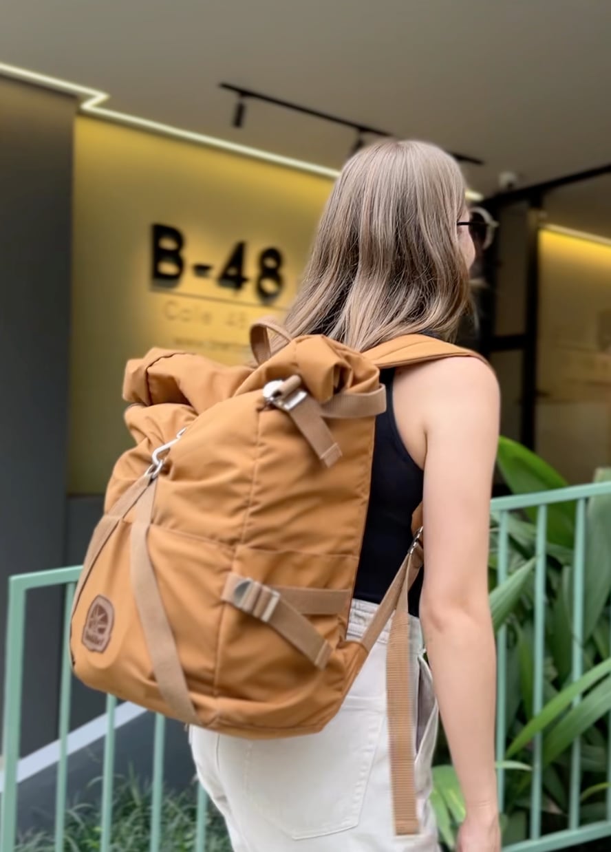 A person is seen walking away from the entrance of B48 Living, carrying a brown backpack. The modern building's signage and soft lighting are visible in the background, while lush greenery frames the scene, contributing to a welcoming atmosphere.