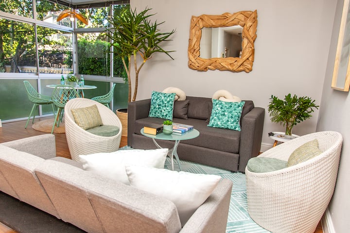 Sala de estar con sofá cama, amplios asientos y TV inteligente de pantalla plana. Grandes ventanales dan al jardín.
