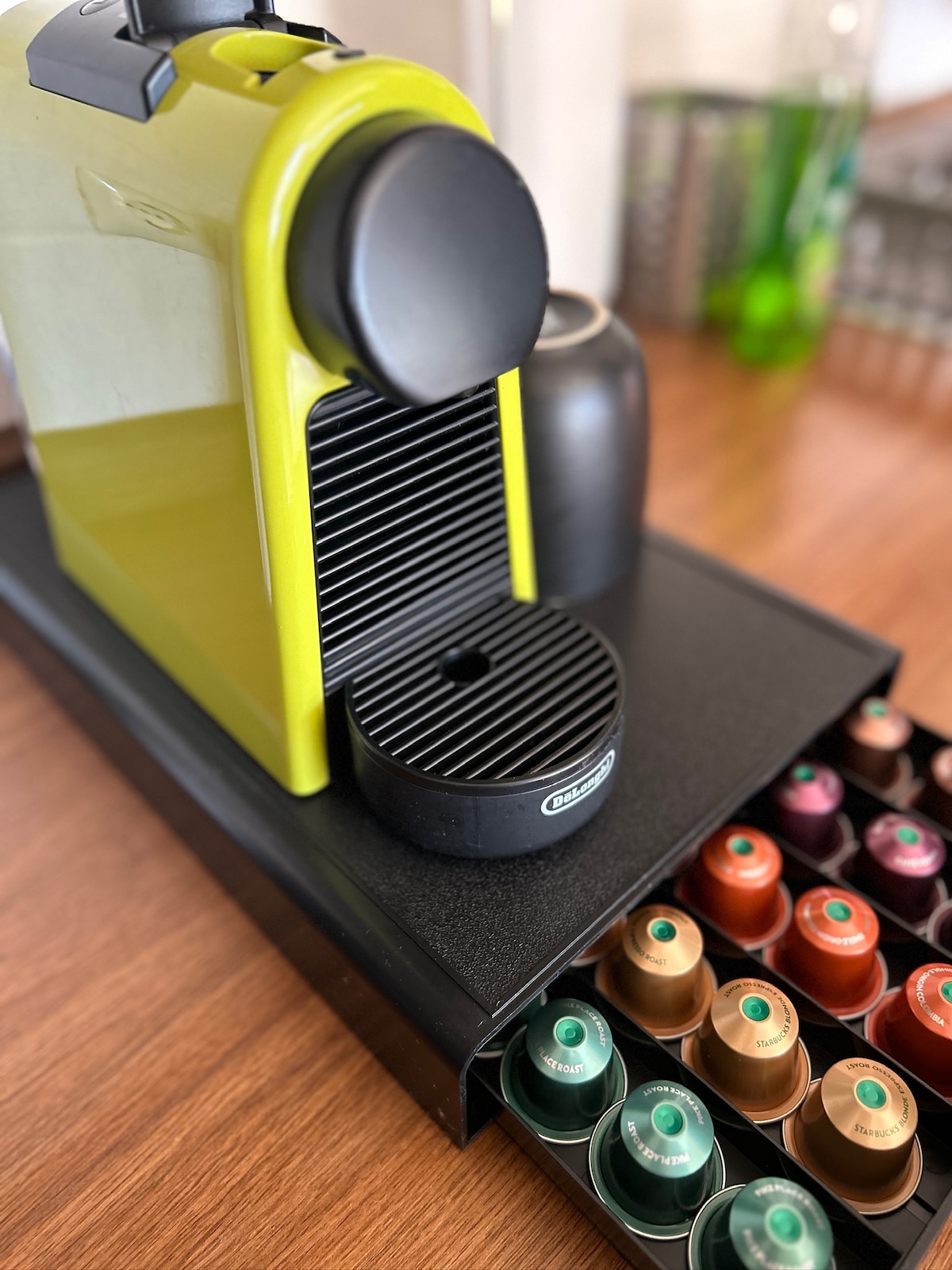 A modern Nespresso machine in a vibrant green color is positioned on a sleek wooden surface. A selection of coffee capsules in various colors is neatly stored in a holder. The design emphasizes functionality and ease of access.