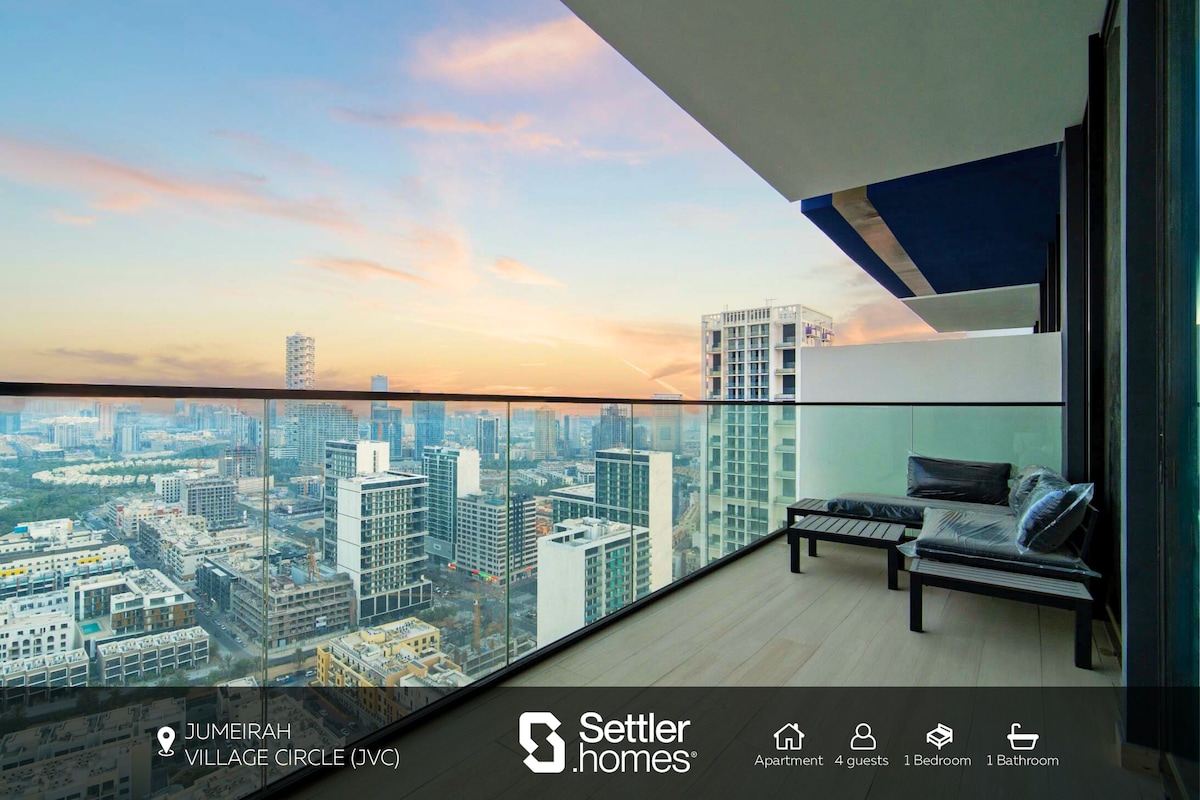 A private balcony on the 29th floor features a modern seating area overlooking the city skyline. The expansive glass railing provides unobstructed views of the surrounding area, with soft lighting from the setting sun creating a serene atmosphere.