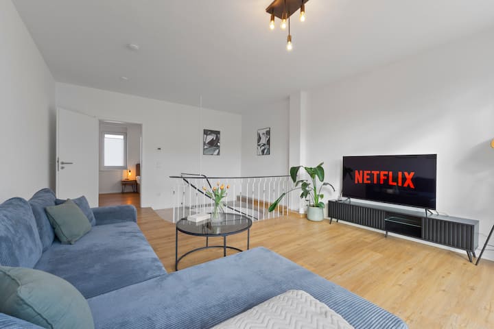 Cozy living area with large sofa, stylish interior and smart TV with Netflix – perfect for relaxing evenings after a day in Bad Kreuznach.
