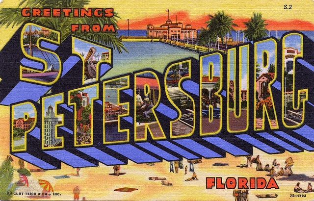 A vintage postcard features bold, colorful letters spelling 'Greetings from St. Petersburg, Florida.' The background depicts a beach scene with people enjoying the sun and water, framed by palm trees and a distant view of a pier.