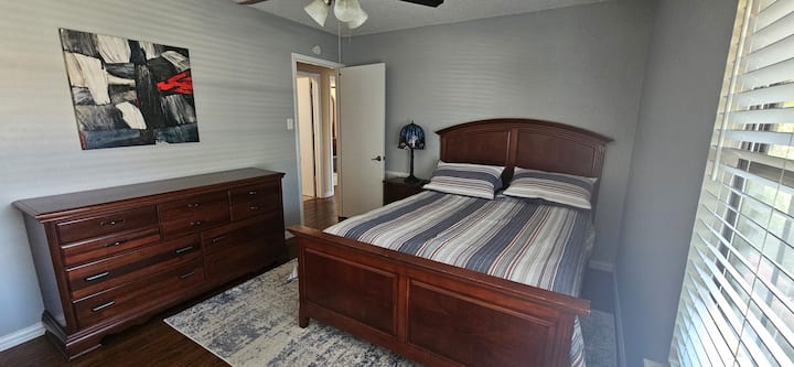 ห้องนอนผู้เข้าพักมีเตียงขนาดควีนไซส์ตู้เสื้อผ้าพัดลมเพดานทีวี Roku โต๊ะข้างเตียงตู้เสื้อผ้าและมู่ลี่  