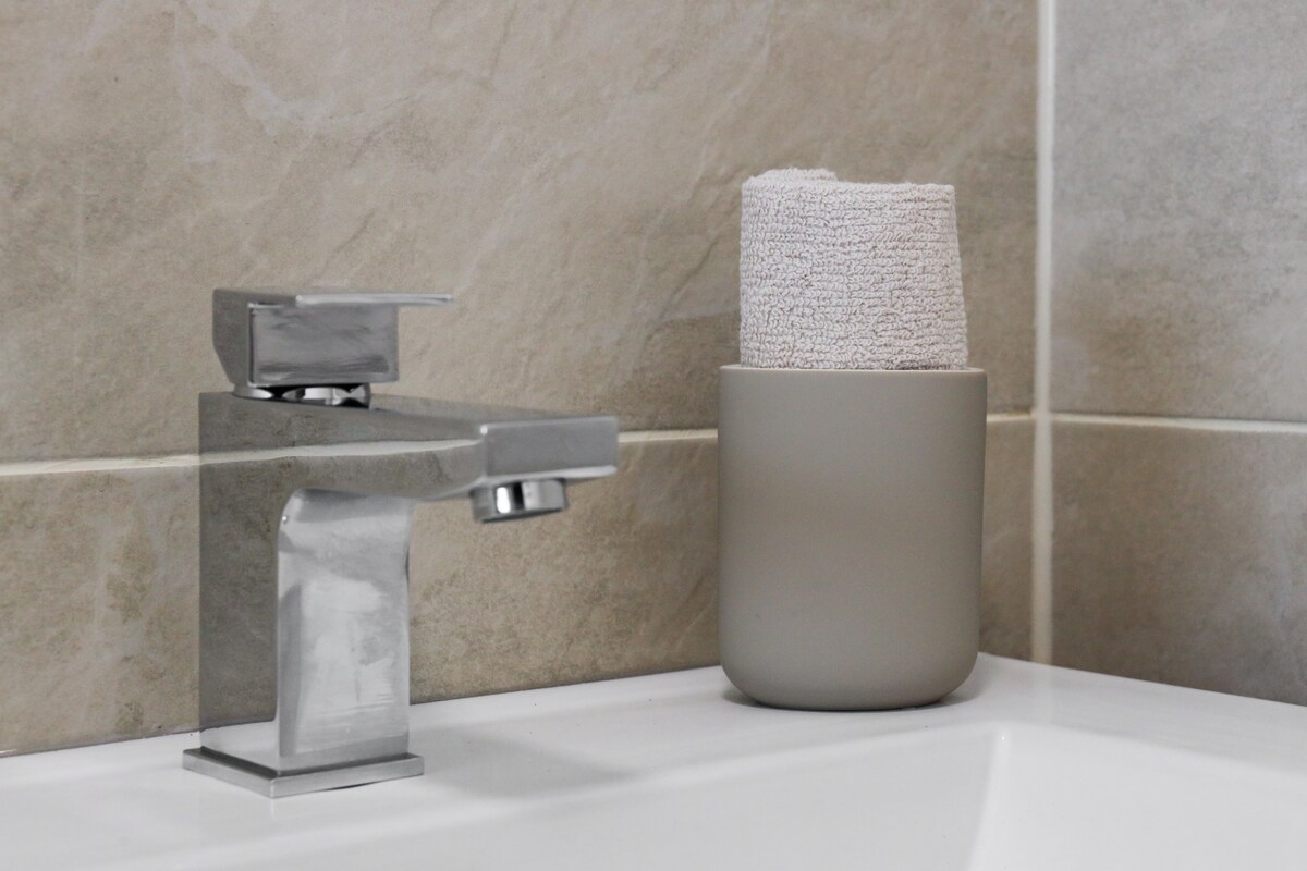 A modern bathroom sink features a sleek chrome faucet beside a soft, textured towel placed in a minimalist grey holder. The neutral-toned tiles create a clean and soothing environment.
