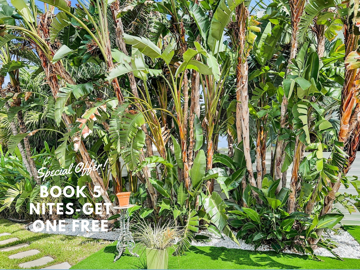 Lush tropical landscaping features towering palms and vibrant greenery in the backyard, creating a private oasis. A well-maintained lawn and a decorative outdoor feature are visible, inviting relaxation and enjoyment of the natural surroundings.