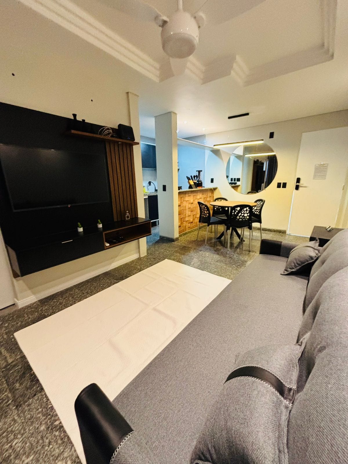 A cozy living area features a comfortable sofa and a flat-screen TV mounted on a modern accent wall. A dining table with stylish chairs is situated nearby, while an integrated kitchen area can be seen in the background, showcasing convenient access to a functional layout.