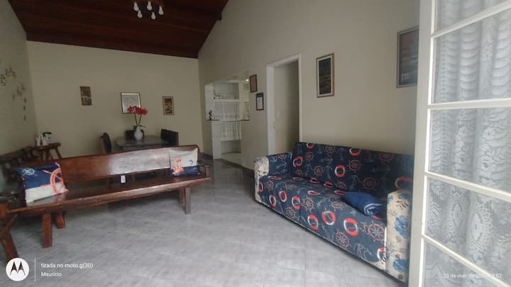 Sala ampla com 02 ambientes, sofá de 04 lugares com capa protetora, 01 banco com 04 lugares de madeira, 02 bancos com 02 lugares de madeira, 04 almofadas.