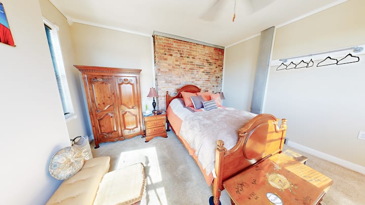 The perfect escape to dreamland is our open & airy main bedroom with Steelers bedtable, heavy vintage furniture, corner nook, matching wooden wardrobe, dresser, bed step, & nightstands, brick backsplash, & extra added space for hanging your clothes!