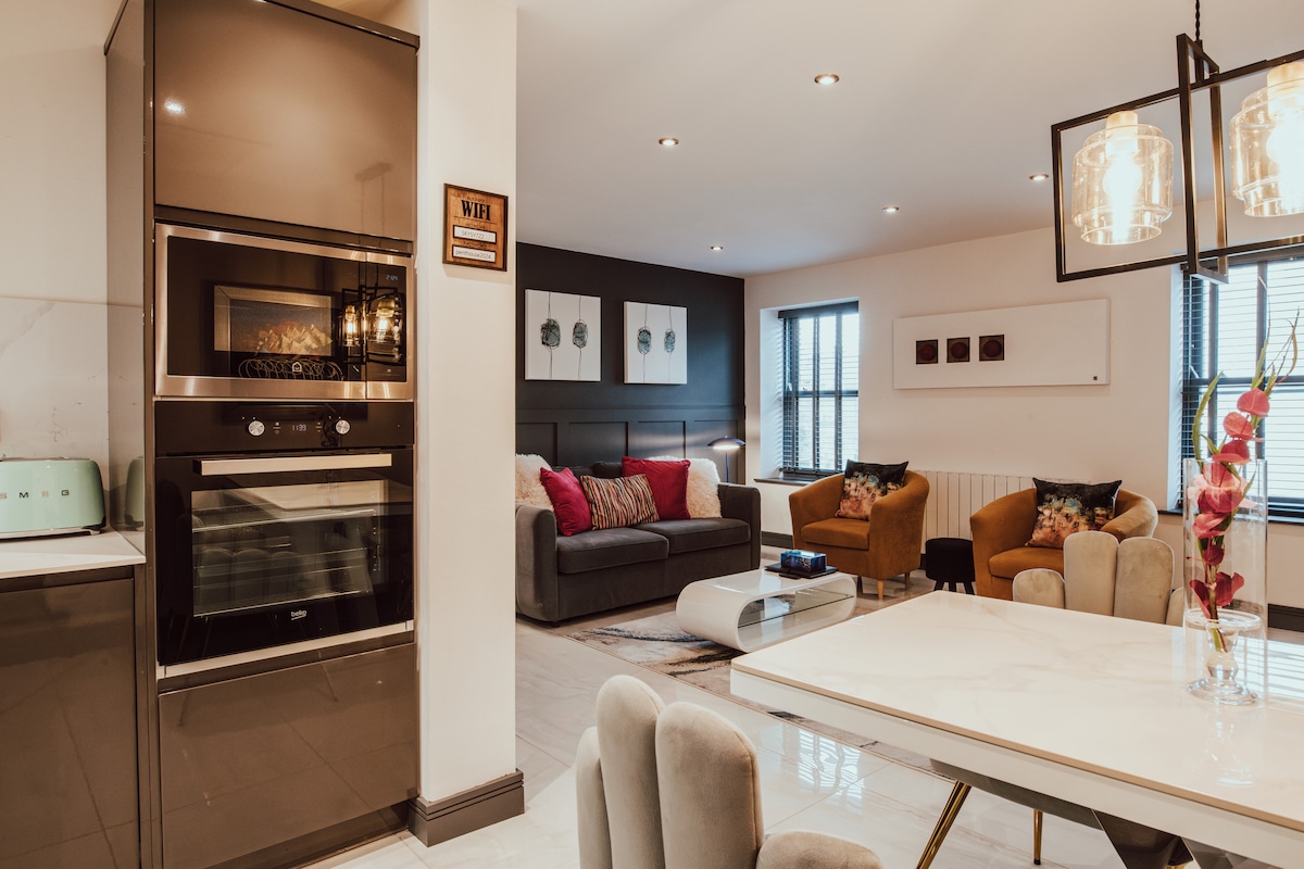 An open-plan living space features modern furnishings, including a cozy sofa and armchairs, surrounded by soft lighting. A spacious dining area with a marble table and upholstered chairs complements a sleek kitchen with stainless steel appliances. Artwork adorns the walls, adding a touch of style.