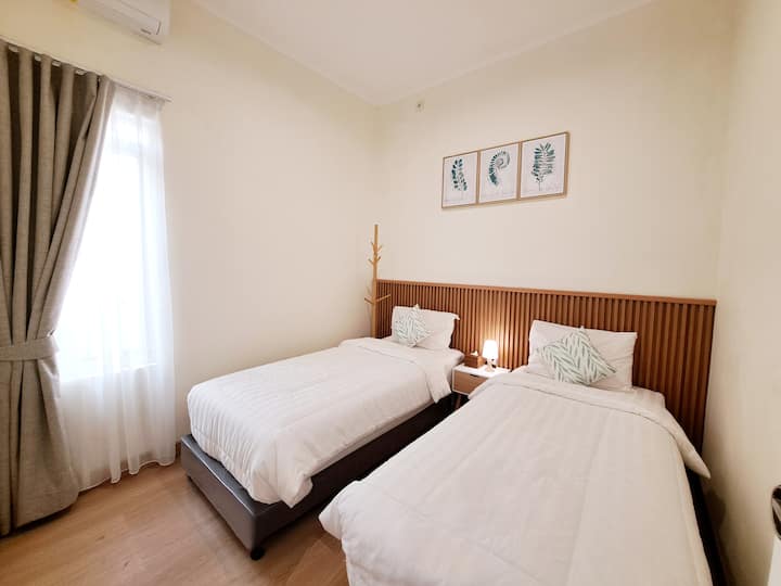 Spavaća soba 2 s dva kreveta za jednu osobu i prozorom s kojeg se pruža pogled na ukrasni zid.