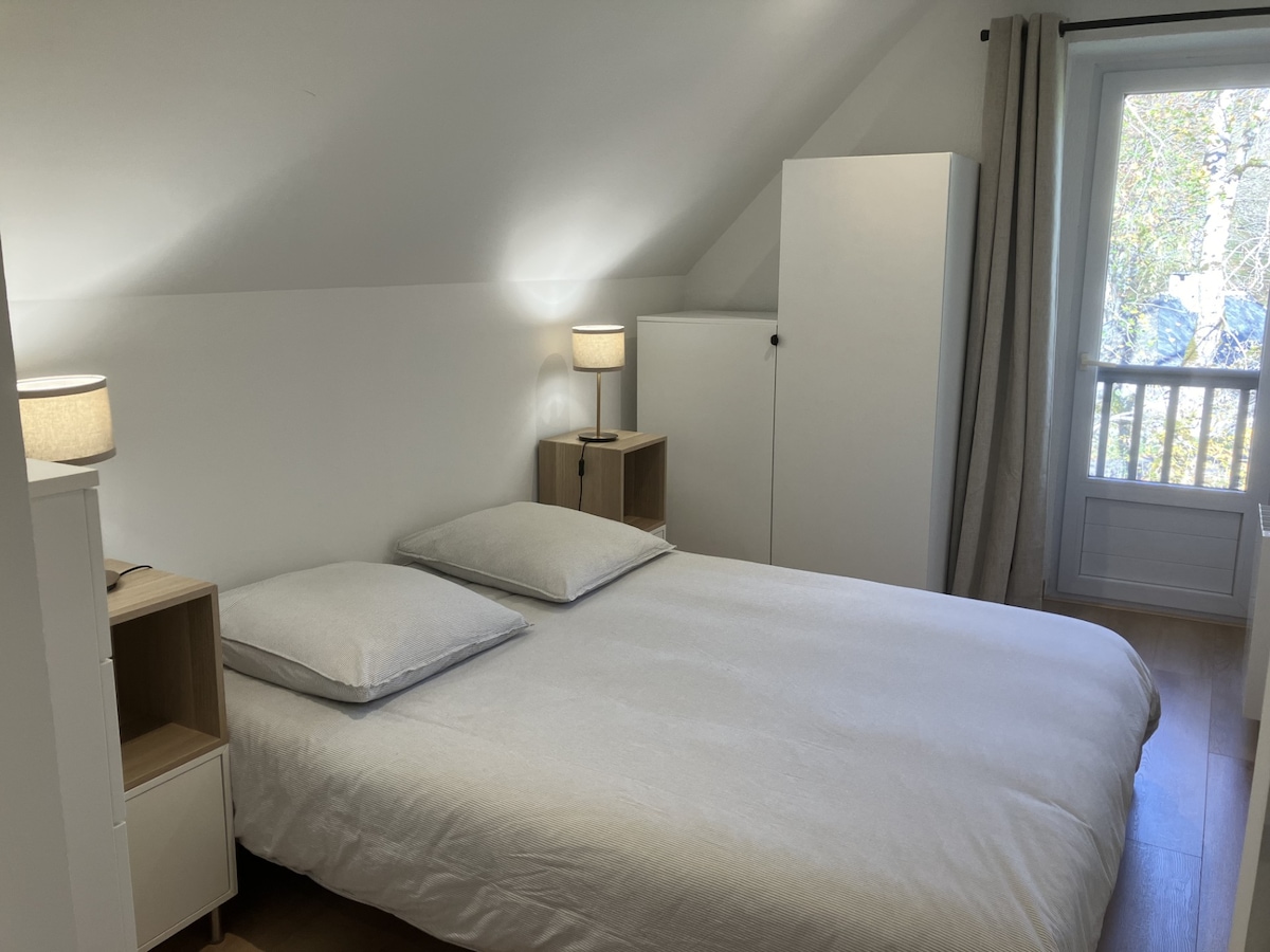 Chambre 2 : Une chambre lumineuse avec un lit Queen Size (160 x 200), encadré par deux lampes de chevet. La porte-fenêtre offre une belle vue sur l’extérieur, apportant de la clarté et une atmosphère apaisante.