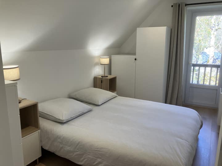 Chambre 2 : Une chambre lumineuse avec un lit Queen Size (160 x 200), encadré par deux lampes de chevet. La porte-fenêtre offre une belle vue sur l’extérieur, apportant de la clarté et une atmosphère apaisante.