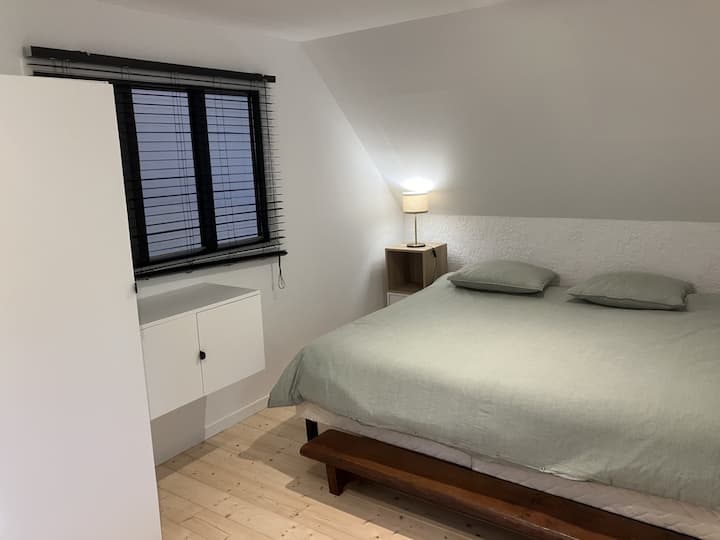 Chambre 1 : Une chambre épurée avec un grand lit King Size (200 x 200), offrant confort et espace. La lampe de chevet apporte une touche chaleureuse pour des nuits paisibles.