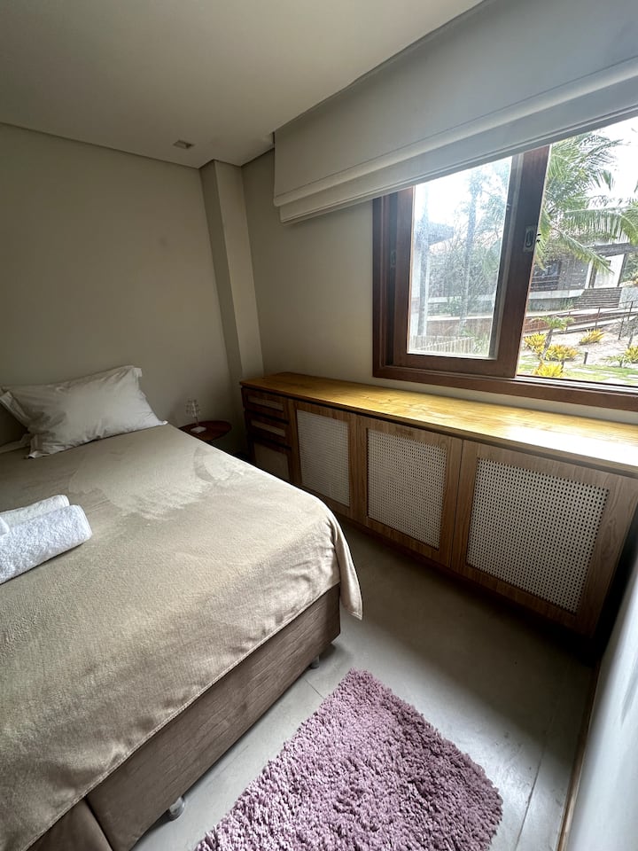 "Quarto aconchegante com tons suaves, toques de madeira e uma grande janela com luz natural. Perfeito para noites tranquilas em Maraú, Bahia."