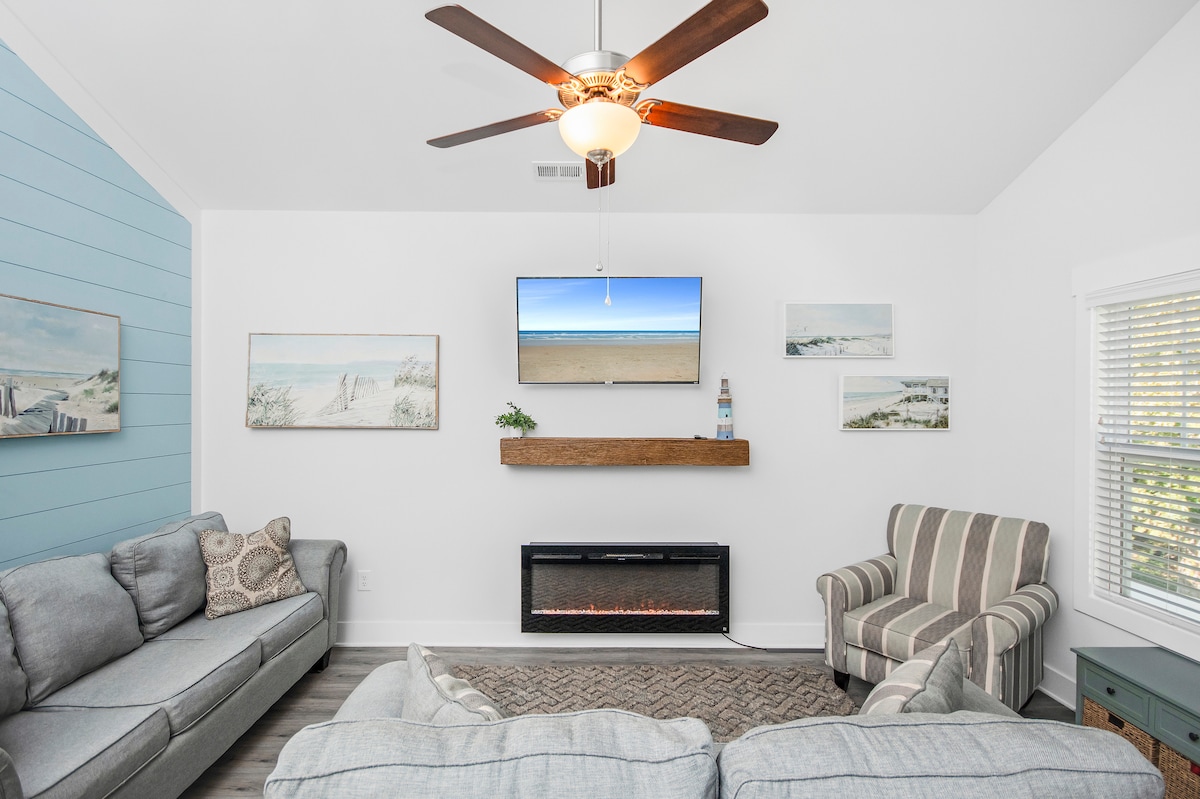 Დაისვენეთ ამ მყუდრო მისაღებ ოთახში, რომელშიც დგას ორი ნაცრისფერი დივანი და თანამედროვე ბუხრის თავზე დამაგრებული ბრტყელეკრანიანი ტელევიზორი. Პლაჟის თემატიკის დეკორი დამამშვიდებელ გარემოს ქმნის, რომელიც იდეალურია განტვირთვისთვის ერთი დღის შემდეგ. Ეს მიმზიდველი ადგილია ოჯახის წევრებისა და მეგობრებისთვის.