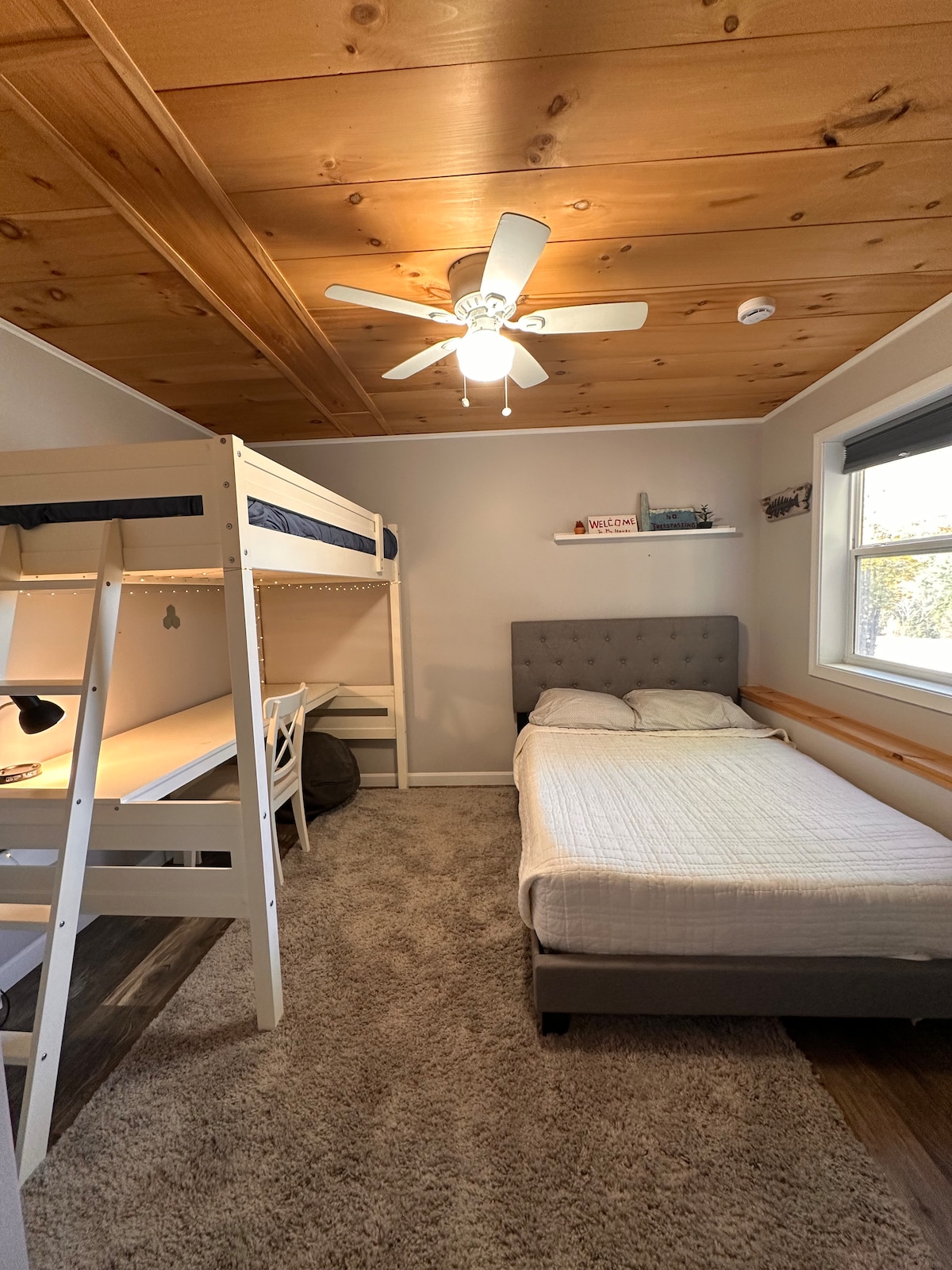 Spavaća soba na nižoj razini s bračnim krevetom i krevetom na kat iznad radnog stola. 