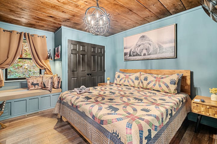 The main floor bedroom features a king bed, end tables, a cozy reading nook, a closet, blackout curtains, and a Roku TV. Conveniently located with easy access to the kitchen, living room, and bathroom.