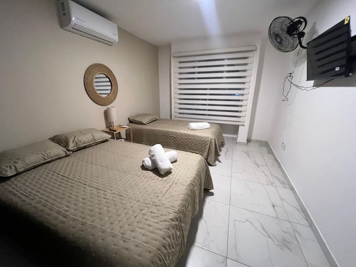 Descansa plácidamente en una habitación fresca y acogedora con dos camas cómodas, matrimonial e individual, aire acondicionado y TV, pensada para brindarte el confort que necesitas después de un día de playa.