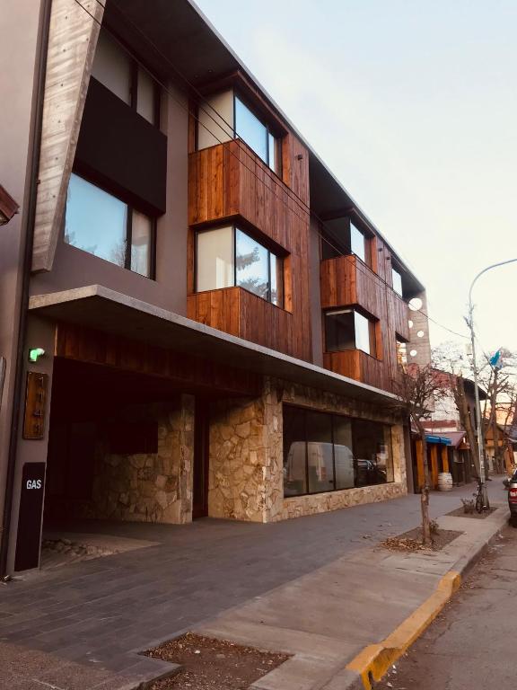 The exterior of the building features a modern design, with a mix of stone and wooden elements. Large windows provide natural light, while balconies add character. A paved walkway leads to the entrance, with street views of the surrounding area.