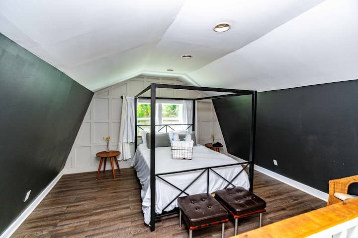 Očarujúca podkrovná spálňa s modernou čiernou posteľou s baldachýnom, mäkkým osvetlením a útulným dekorom. Šikmý strop a zvýraznená stena vytvárajú intímny priestor s hrejivou a príjemnou atmosférou.