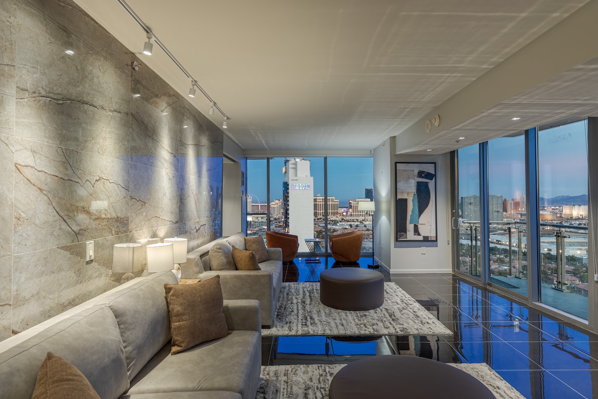 A modern living area showcases sleek furniture against a backdrop of floor-to-ceiling windows offering city views. The space is illuminated by soft lighting, highlighting the elegant marble walls and unique artwork. Cozy seating areas invite relaxation, while the plush textiles add comfort.