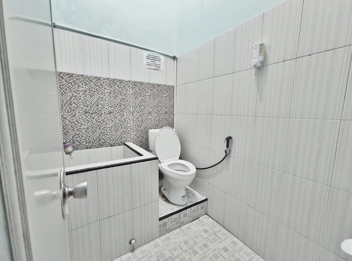 The bathroom features a modern design with wall tiles and a mosaic accent. A white toilet is positioned against the wall, and a shower area is partially visible. A mirror is mounted above the sink, and light fixtures provide ample visibility.