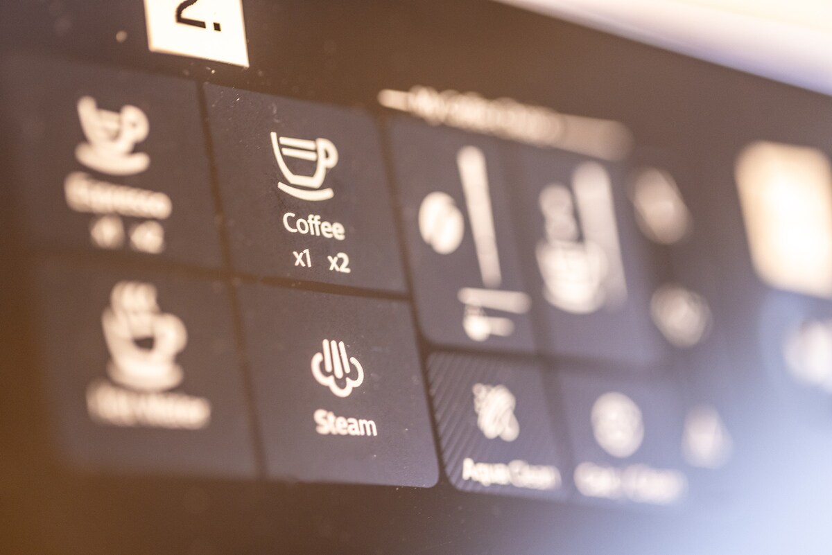 The image showcases a close-up of a coffee machine control panel. It features various buttons including options for espresso, coffee, hot water, and steam. The design is sleek and modern, highlighting a user-friendly interface.