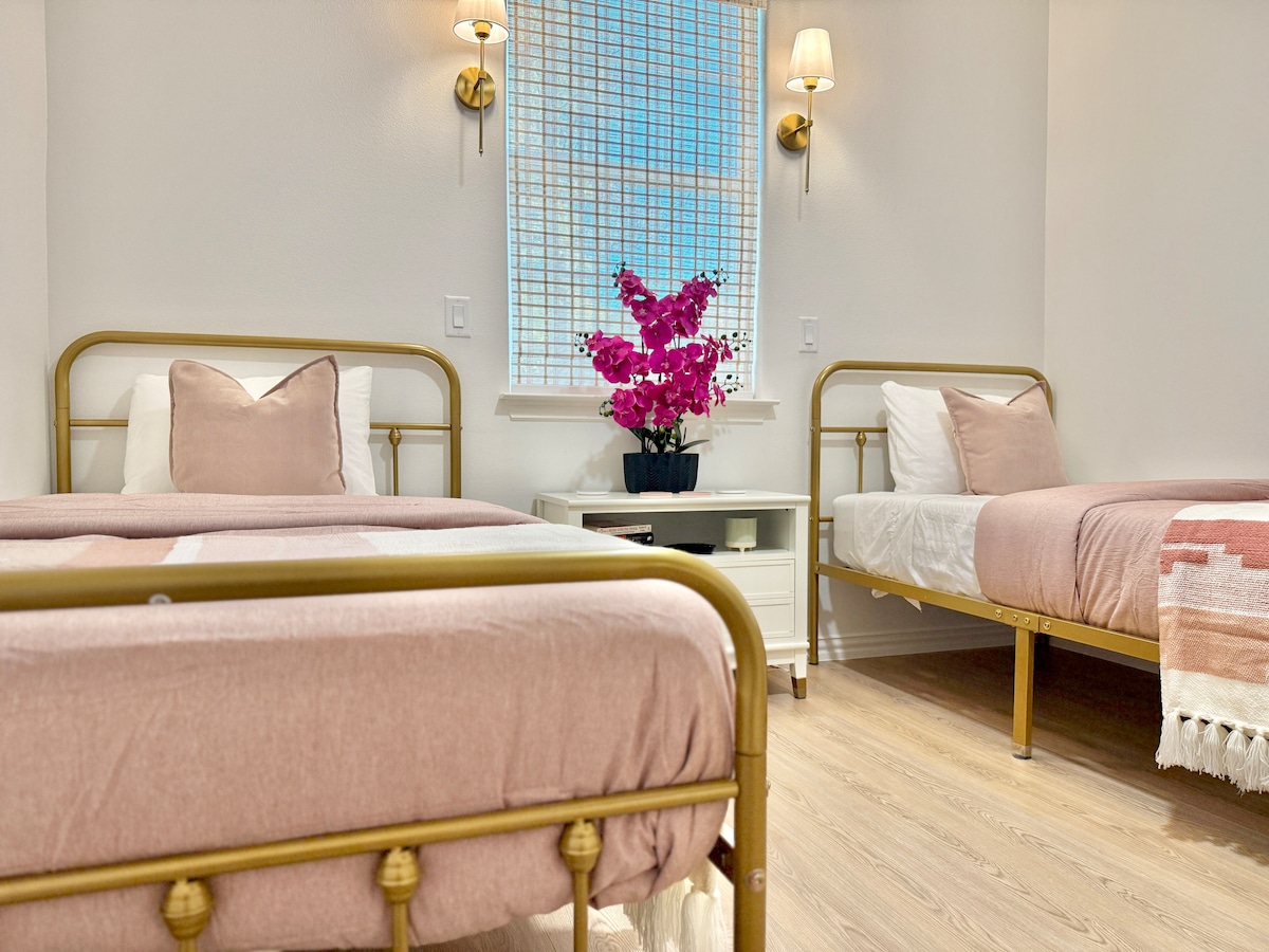Unwind in the charming guest bedroom featuring two cozy twin beds with soft pink covers and fluffy throw blankets. Perfect for friends or family to relax in comfort and style!